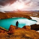 Person standing over Krafla looking into distance, blue water
